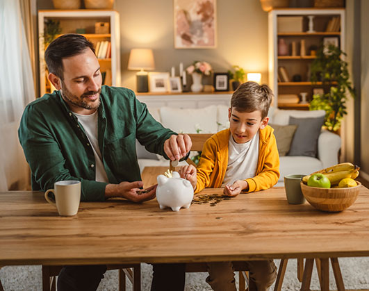 Father and son putting coins in piggy bank
