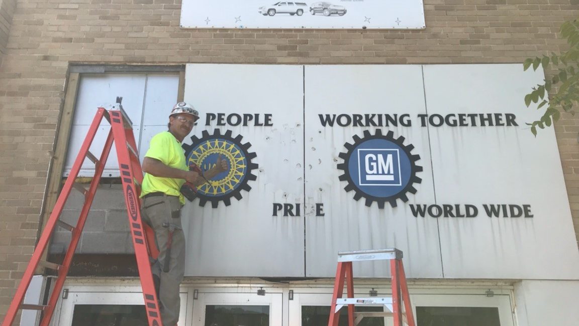 Ken Kueng, senior superintendent at JP Cullen, the construction firm that built the GM plant in 1919 and is now building the Legacy Center, removing the sign from the front entrance of the GM plant that will be displayed at the Legacy Center.